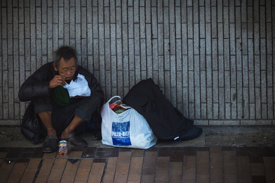 Elderly man sitting on city street, surrounded by bags, conveying solitude.